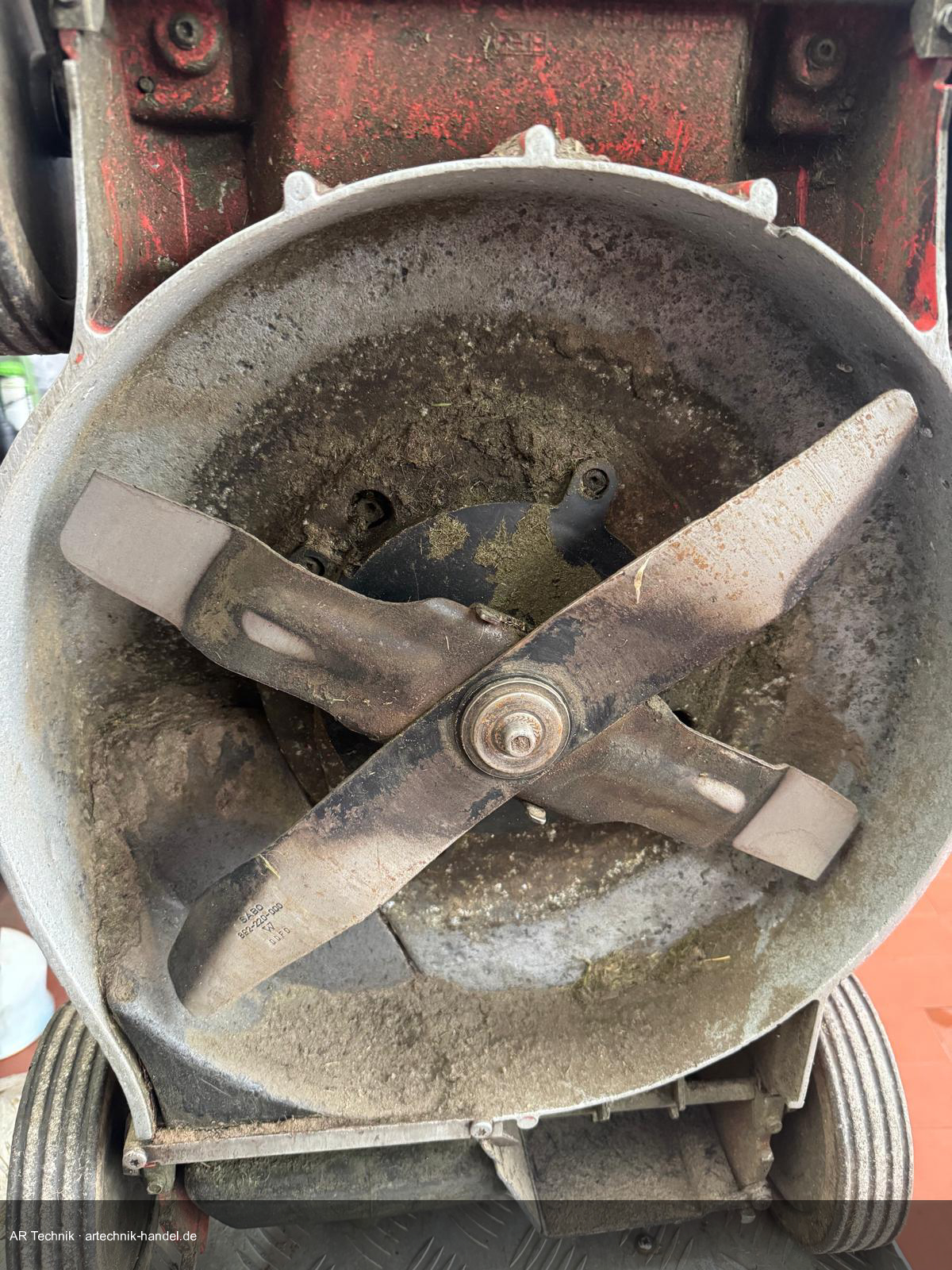 Rasenmäher-Mähwerk von unten – 4-Flügel-Mulchmesser mit eingetrocknetem Grasschnitt verklebt
